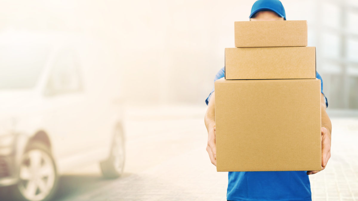 delivery man holding pile of cardboard boxes in front